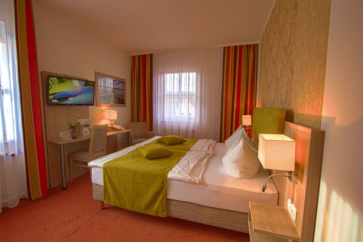 Ein Hotelzimmer mit Bett, Schreibtisch, Stuhl, Fernseher und einem Fenster mit Vorhängen.