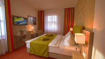 Ein Hotelzimmer mit Bett, Schreibtisch, Stuhl, Fernseher und einem Fenster mit Vorhängen.