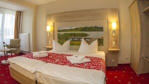 A hotel room with a large bed, two bedside lamps, a painting of a lake, a chair, and a small table. - Seehotel Plau Am See (Plau am See)