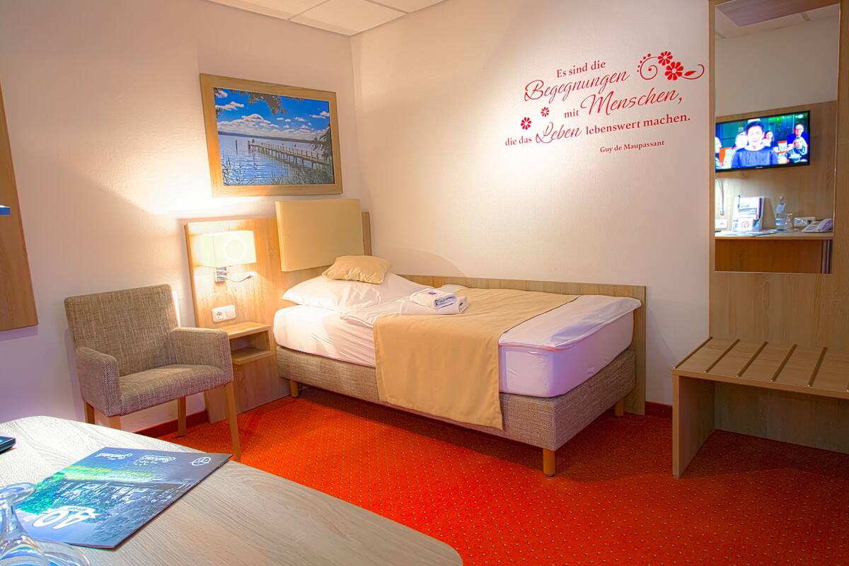 Ein Hotelzimmer mit Bett, Sessel, Schreibtisch, Fernseher und Wanddeko.