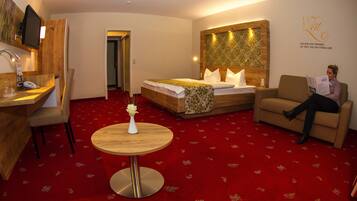 Ein Hotelzimmer mit Bett, Schreibtisch mit Telefon, Stuhl, rundem Tisch mit Vase sowie Wand mit Dekoration und Text.