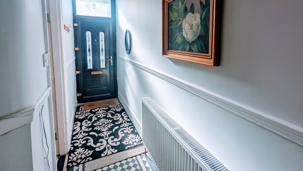 A hallway with a patterned floor, a black door with glass panels, a framed picture on the wall, and a radiator. - TopHome Finsbury Park (London)