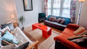 A living room with a sofa, a red coffee table, a TV, and a window with curtains. - TopHome Finsbury Park (London)