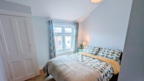 A bedroom with a bed, a window with curtains, a nightstand with a lamp, and a door. - TopHome Finsbury Park (London)