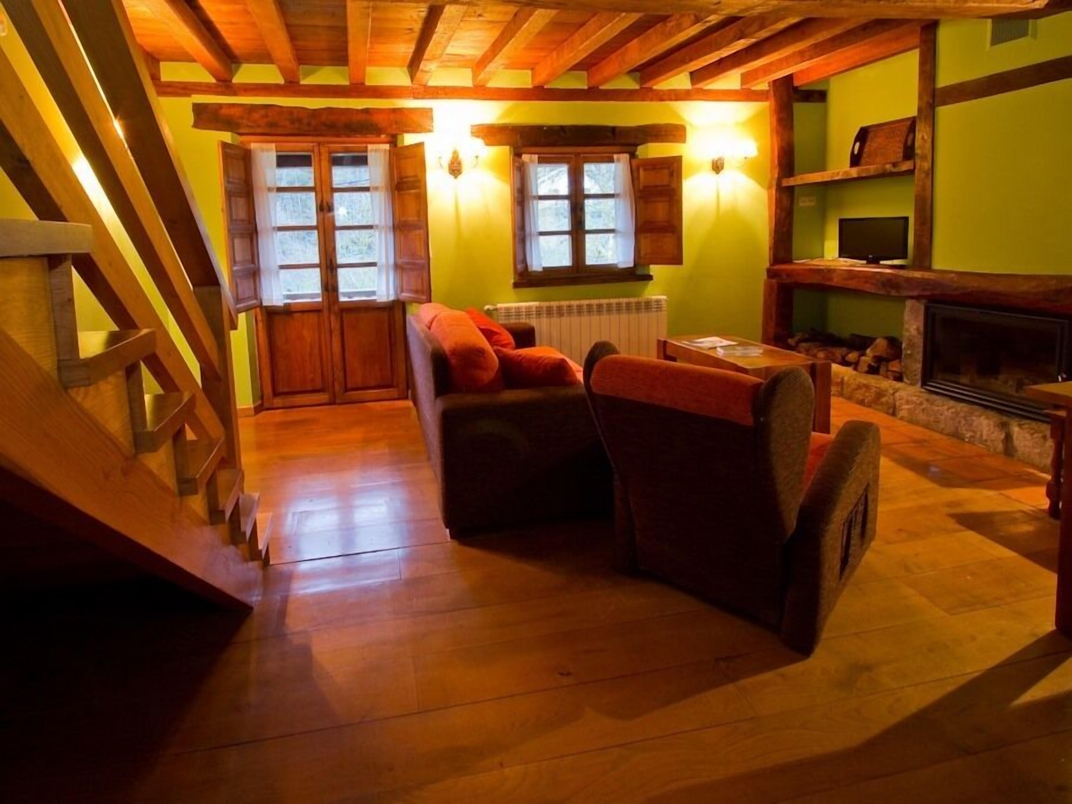 A cozy room with wooden beams, a fireplace, and a seating area with two armchairs and a small table.