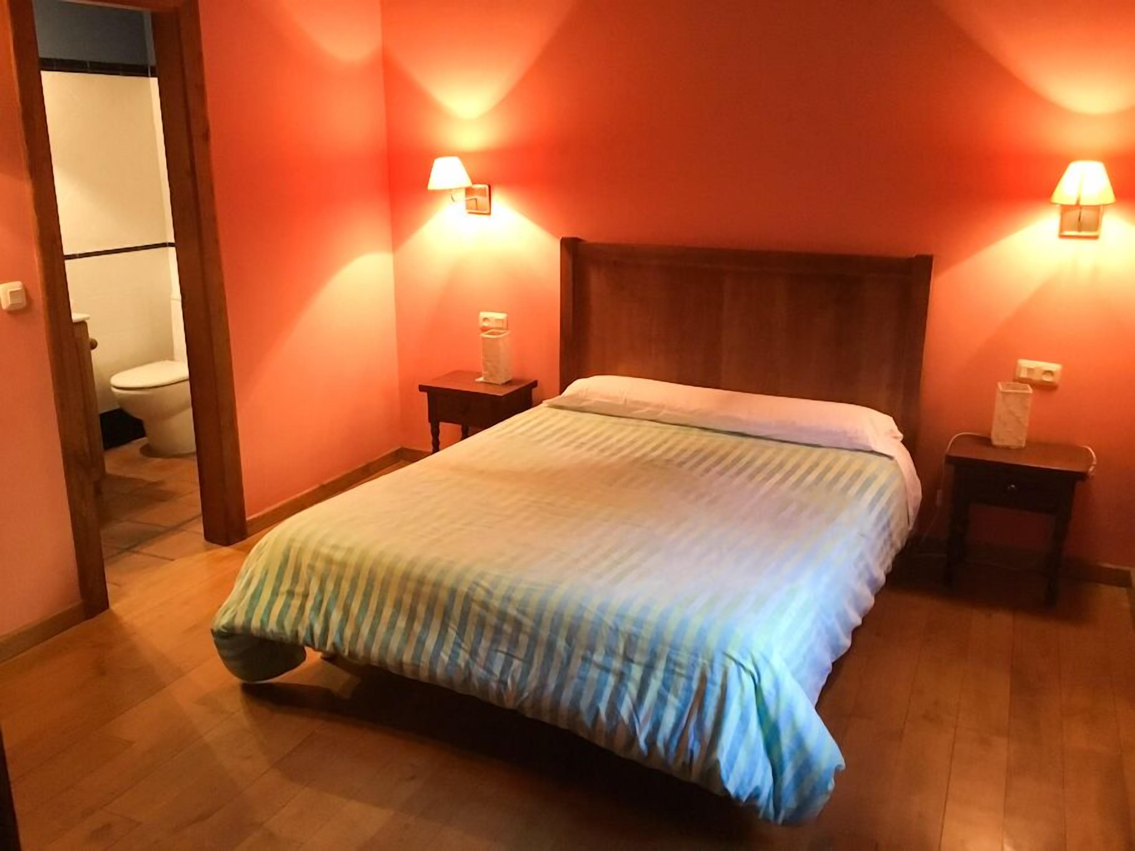 Quarto de hotel com cama de madeira, duas mesas de cabeceira e um criado-mudo.