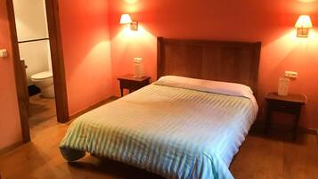Quarto de hotel com cama de madeira, duas mesas de cabeceira e um criado-mudo.
