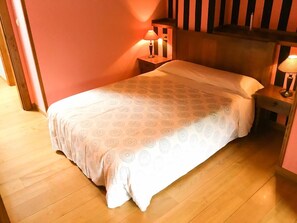 A single bed with a patterned bedspread in a room with wooden flooring and a red wall. There are two bedside tables with lamps. - La Yosa de Argüebanes (Camaleno)