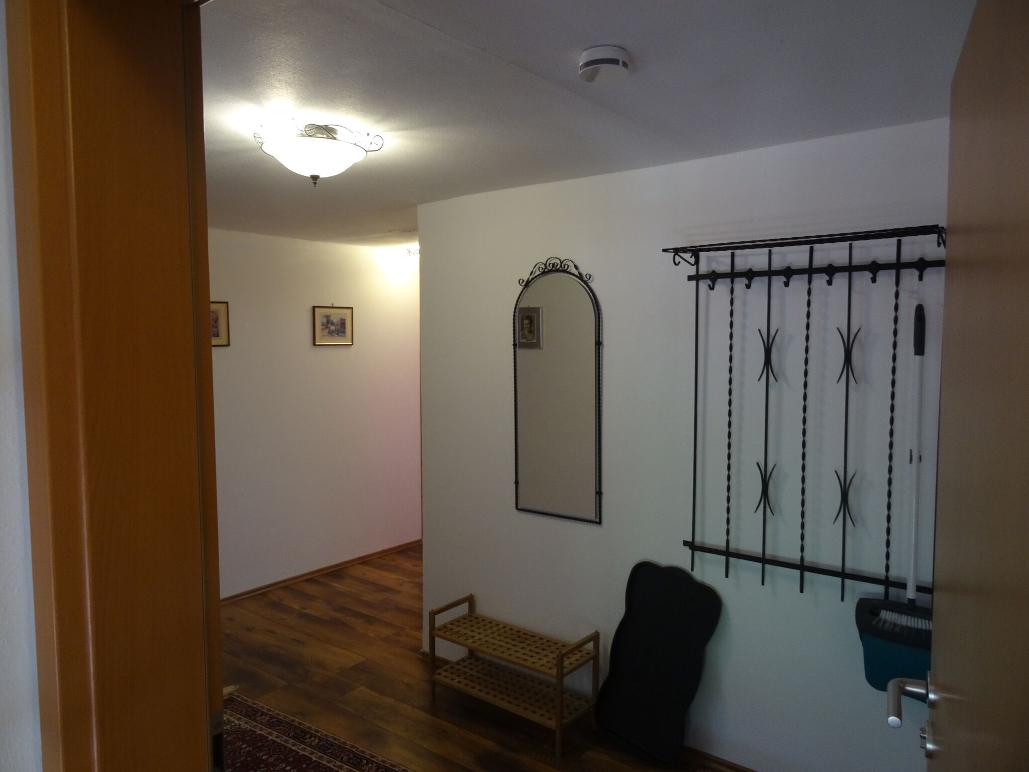 A hallway with wooden flooring, a bench, a mirror, and a wall-mounted rack with cleaning supplies.