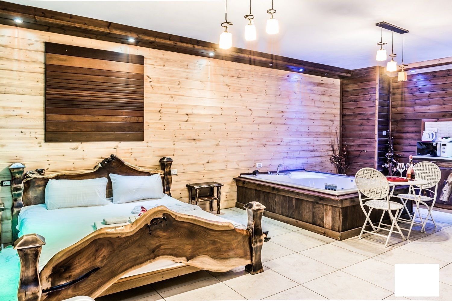 A wooden cabin-style bedroom with a large bed, a hot tub, and a dining area with chairs.