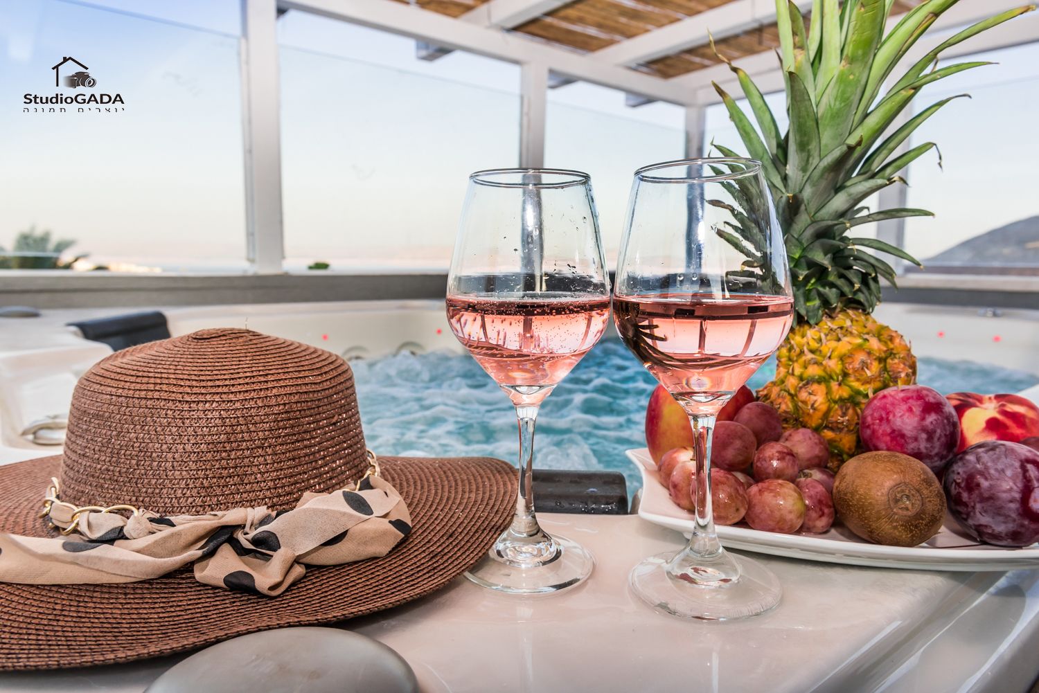 Ein Tisch mit zwei Weingläsern, einem gewebten Hut und einer Fruchtschale in Poolnähe.
