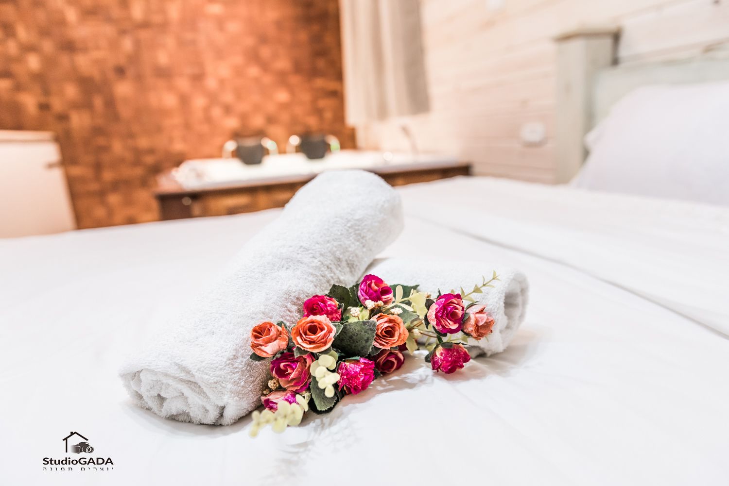 A neatly made bed with a white towel and a bouquet of flowers.