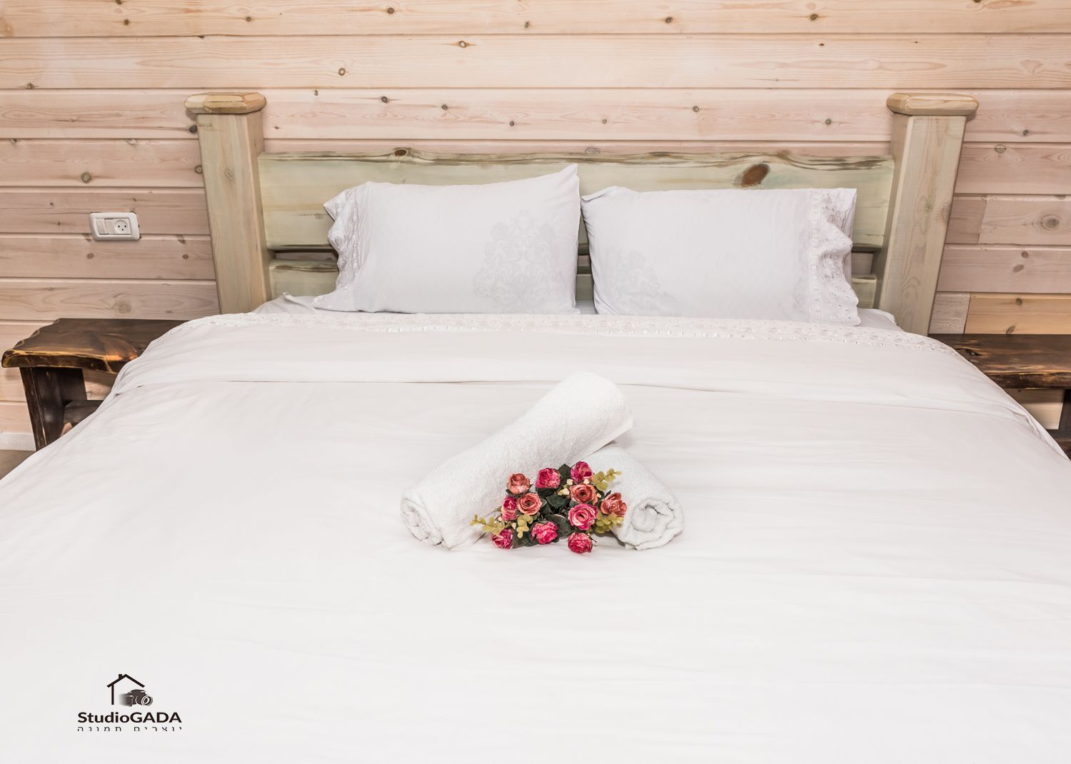 Una cama bien hecha con sábanas blancas y una toalla enrollada con un ramo de flores rosadas.