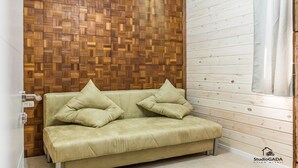 Quarto com parede em padrão herringbone de madeira, sofá bege com almofadas e janela com cortinas.