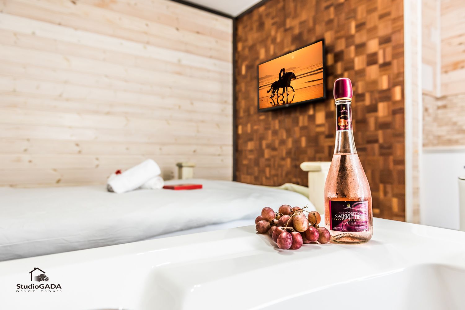 Et hotelværelse med en trævæg, en seng, et billede af en hest og en flaske rosévin på et bord.
