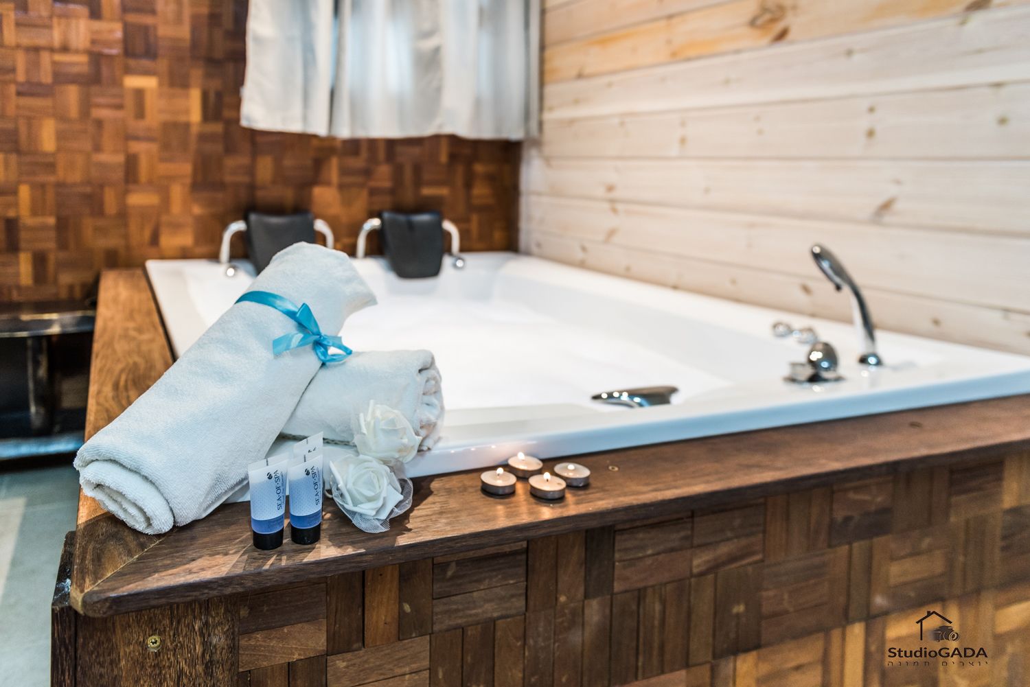 A spa area with a large bathtub, towels, candles, and essential oils on a wooden counter.