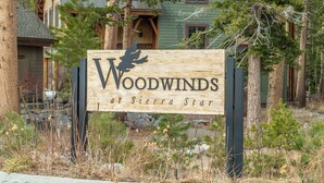 Un panneau en bois portant l’inscription « Woodwinds at Sierra Star », entouré d’arbres, avec un bâtiment en arrière-plan.