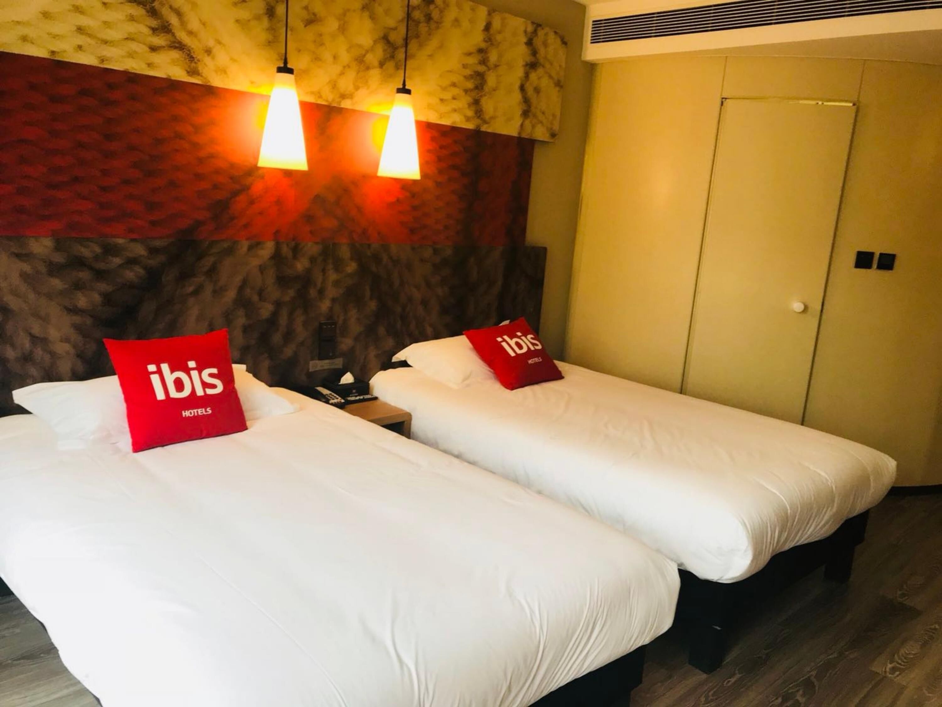 Two single beds with white bedding and red pillows, a marble-patterned wall, and a door with a handle.