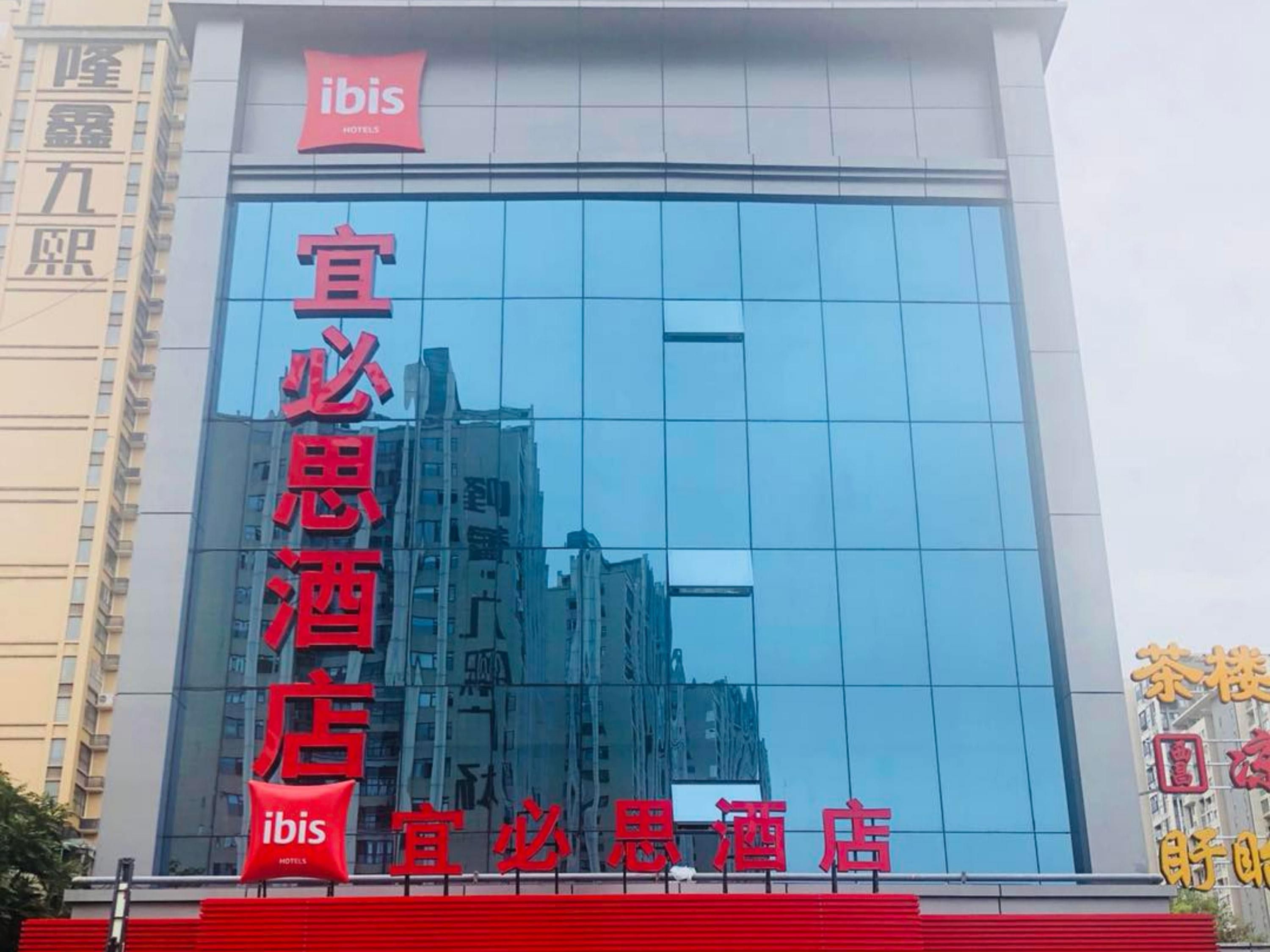 A hotel with a modern glass facade, red signage, and a prominent 'ibis' logo.