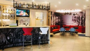 Uma área de bar moderna com televisão, garrafas de vinho e um sofá vermelho ao fundo.