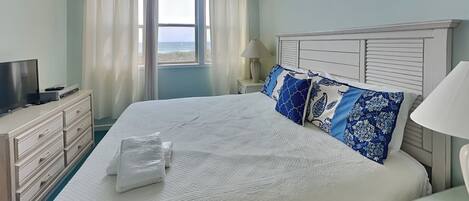 Un dormitorio con una cama grande, un televisor sobre una cómoda y una ventana con cortinas.