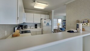 A modern kitchen with white cabinets, a built-in stove, a coffee maker, and a refrigerator. - Sweet Serenity | Oceanfront Townhouse! (Topsail Beach)