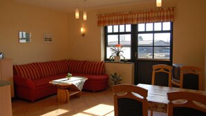 A living room with a sofa, a dining table, chairs, a TV, and a window with a view.