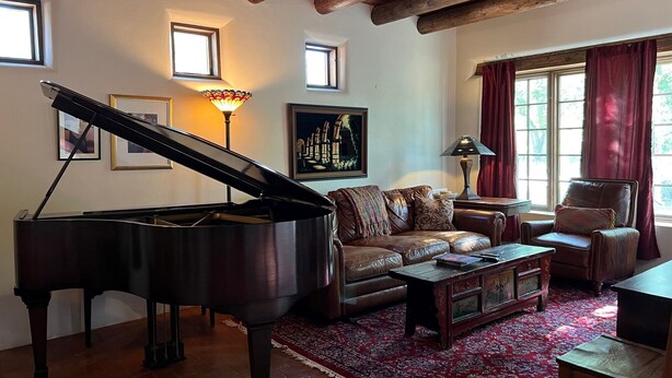 A grand piano in a living room with a red carpet, leather sofas, and a wooden ceiling. - Balloon Fiesta close to Charming, Historic, N. Valley Casita! (Albuquerque)