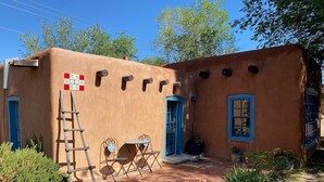 A rustic building with a blue door and window, a small patio with a table and chairs, and a ladder leaning against the wall. - Balloon Fiesta close to Charming, Historic, N. Valley Casita! (Albuquerque)