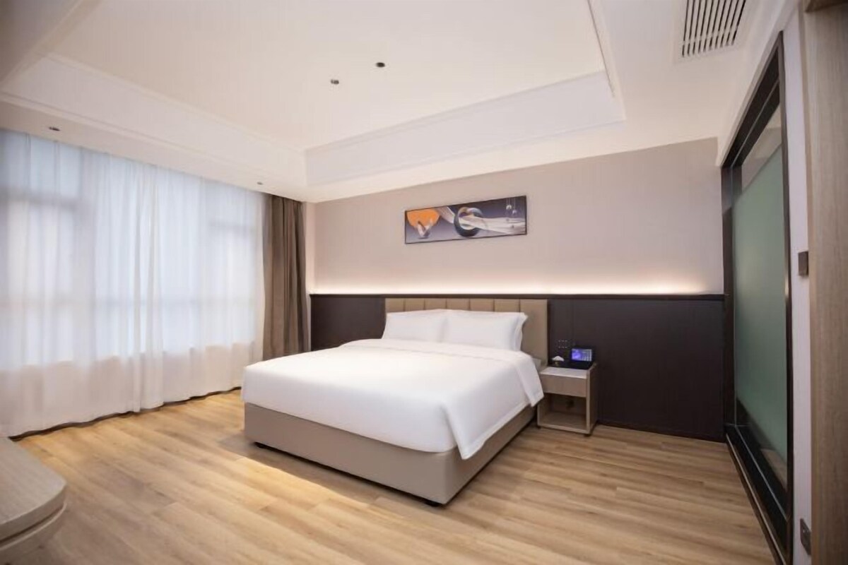 A modern hotel room with a large bed, a bedside table, a TV, and a window with curtains.