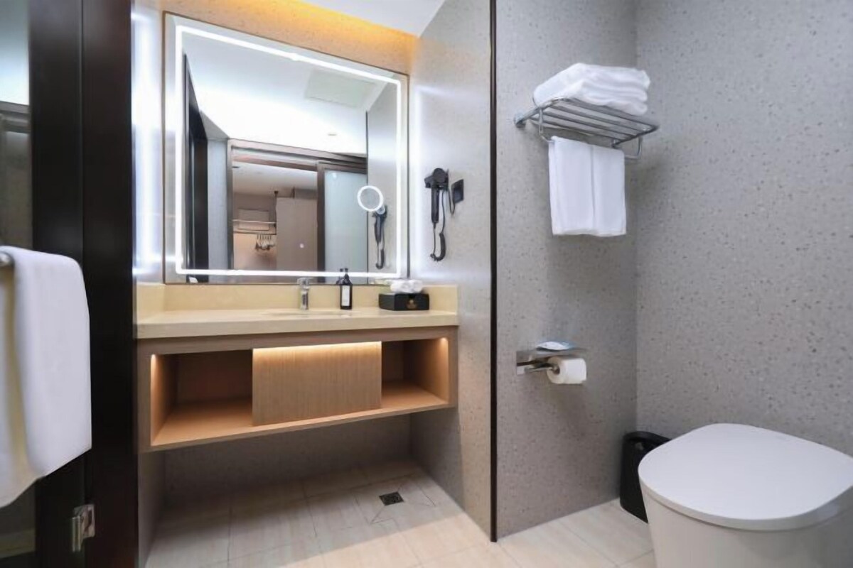 A modern bathroom with a large mirror, vanity, towel rack, and toilet.