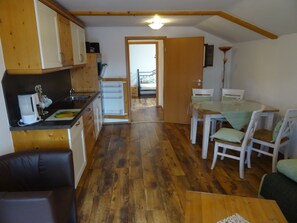 A compact kitchen with wooden cabinets, a refrigerator, and a dining area with a table and chairs.