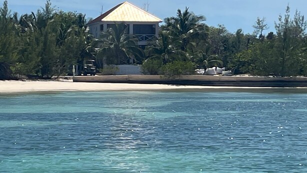 Ein Strandgrundstück mit einem Haus, umgeben von Palmen und einem Sandstrand.