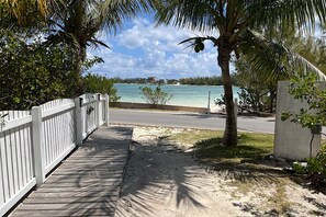 A wooden walkway leading to a beach with a view of the ocean and palm trees. - Island Gypsy | Beachfront 2BR on Coco Bay (Green Turtle Cay)