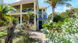 A two-story building with a balcony, surrounded by tropical vegetation.