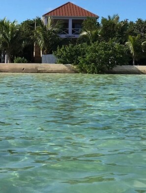 A beachfront property with a house, clear water, and lush greenery.