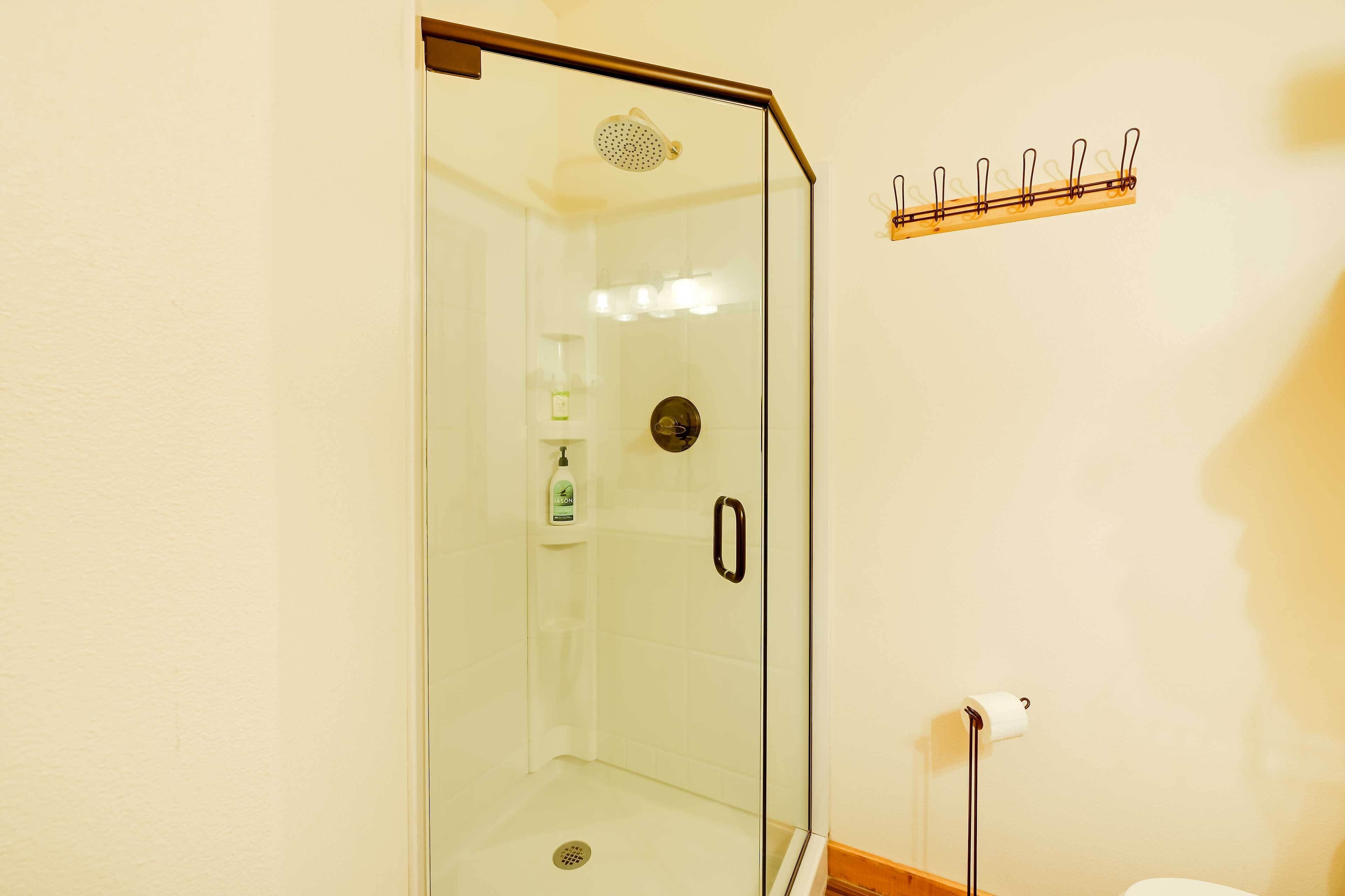 A glass-enclosed shower with a handheld showerhead, a toilet paper holder, and a shelf with toiletries.