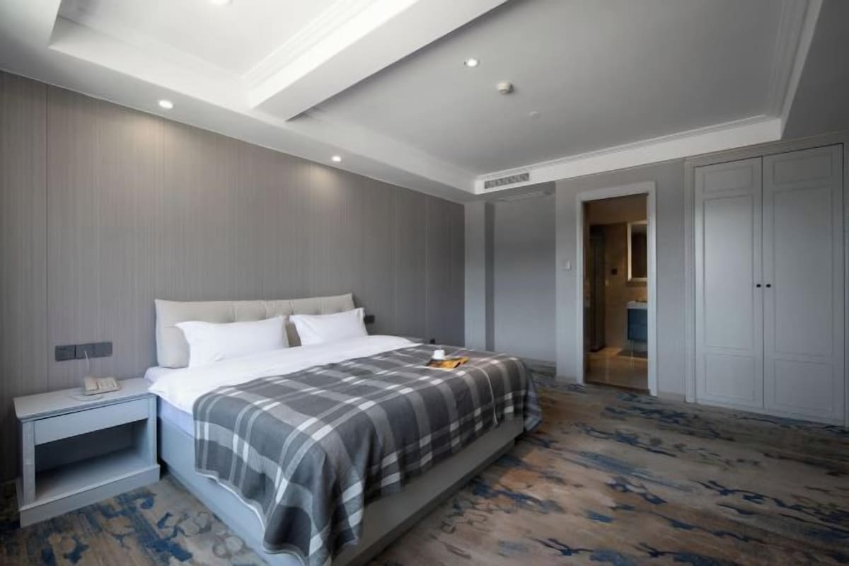 A modern hotel room with a large bed, a nightstand, a wardrobe, and a bathroom visible through an open door.