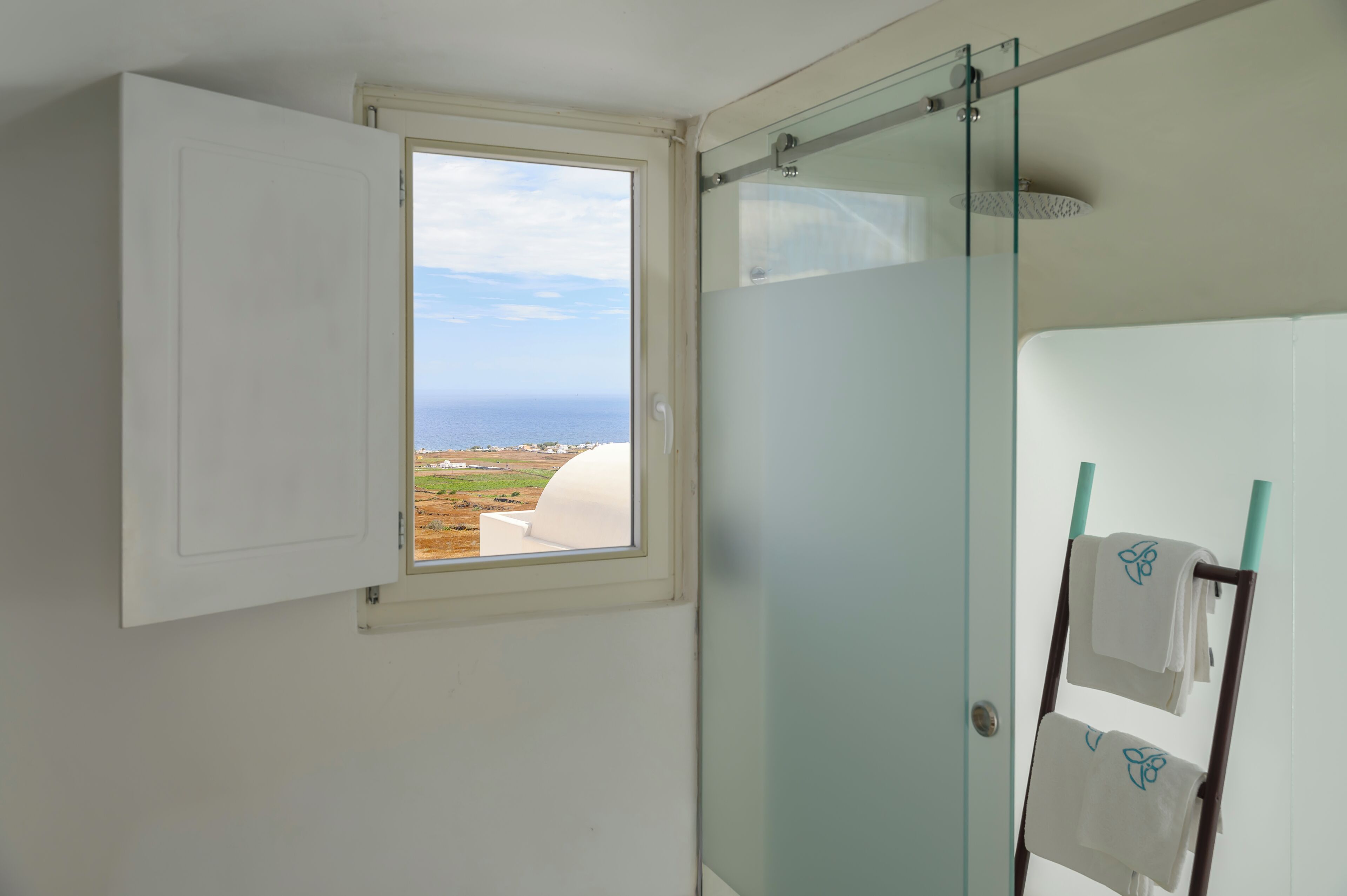 Un baño con mampara de vidrio, toallero y ventana con vistas al mar.