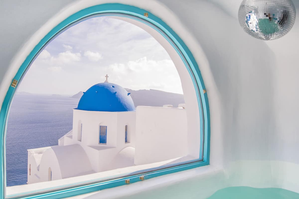 Una habitación con un gran ventanal que da a un edificio de cúpulas azules y al mar.