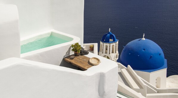 A white-walled building with a blue-domed structure, a small wooden table, and a potted plant. - Sophia Oia View (Santorini)