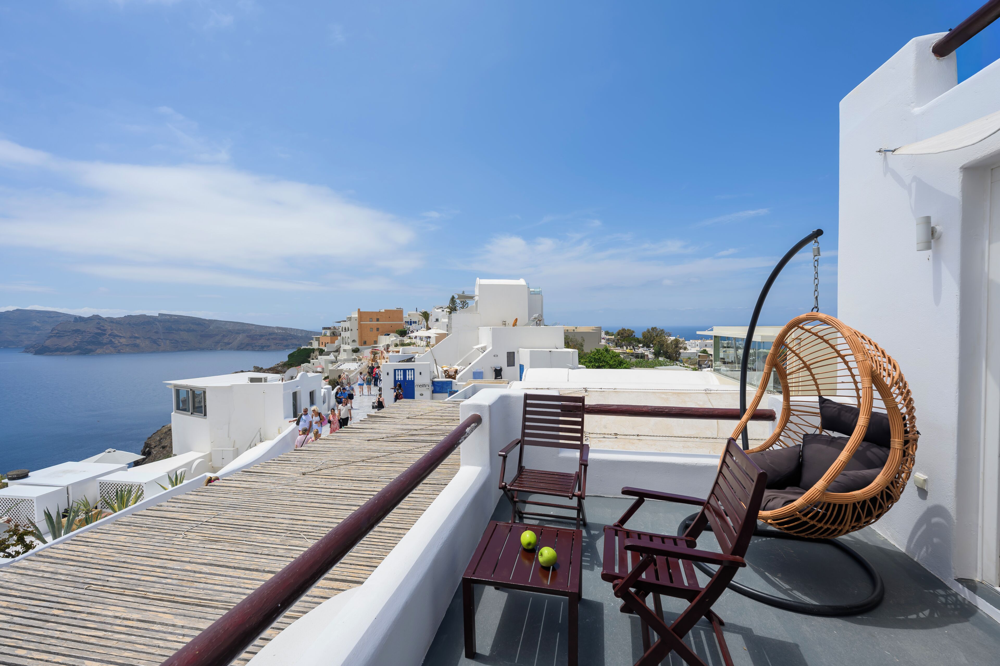 Una terrazza sul tetto con vista sul mare, una sedia in vimini, un tavolo con delle mele e un edificio bianco sullo sfondo.