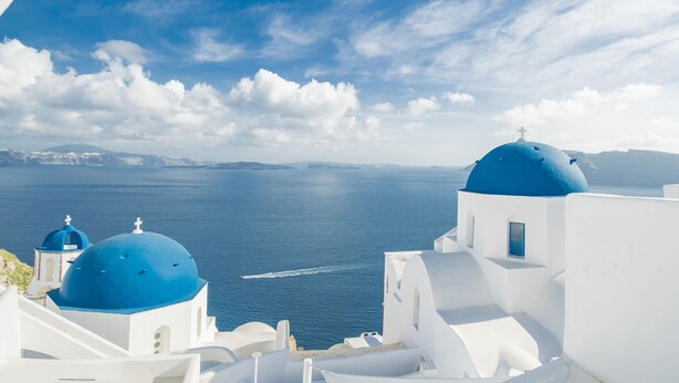A coastal view with white buildings and blue domes, overlooking the sea. - Sophia Oia View (Santorini)