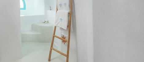 Una habitación con paredes blancas, una escalera de madera apoyada en la pared, un escalón que lleva a una ventana y una toalla colgando en la escalera.