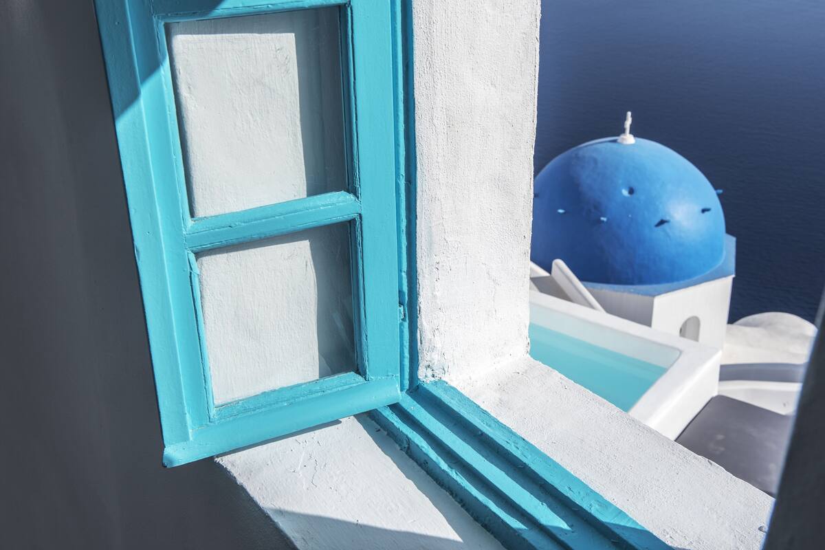 Primer plano de una ventana con marco azul y contraventanas blancas, que da a un edificio blanco con cúpula azul.