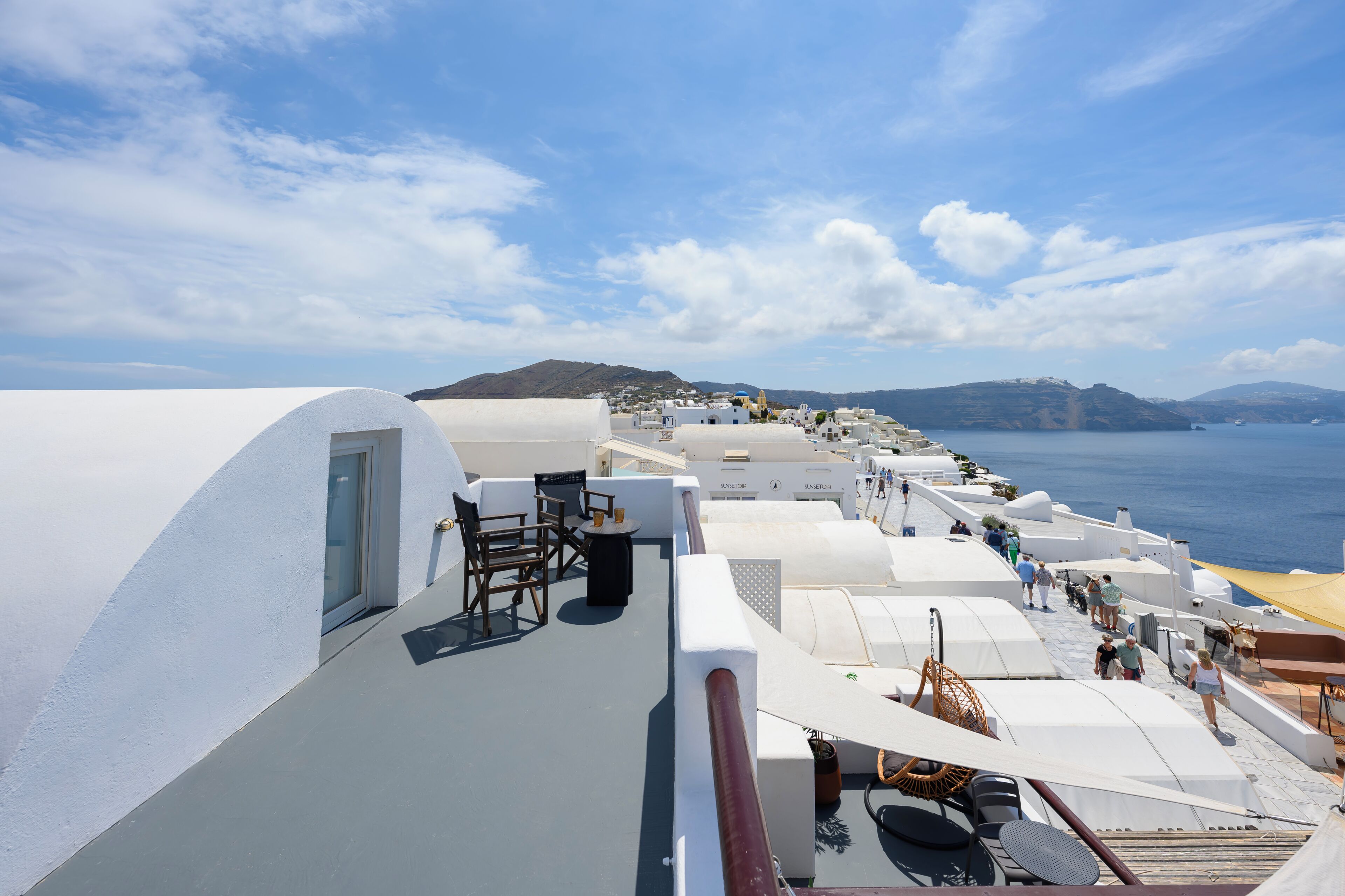 A deck with white railings, sun loungers, and a view of the sea and distant hills.