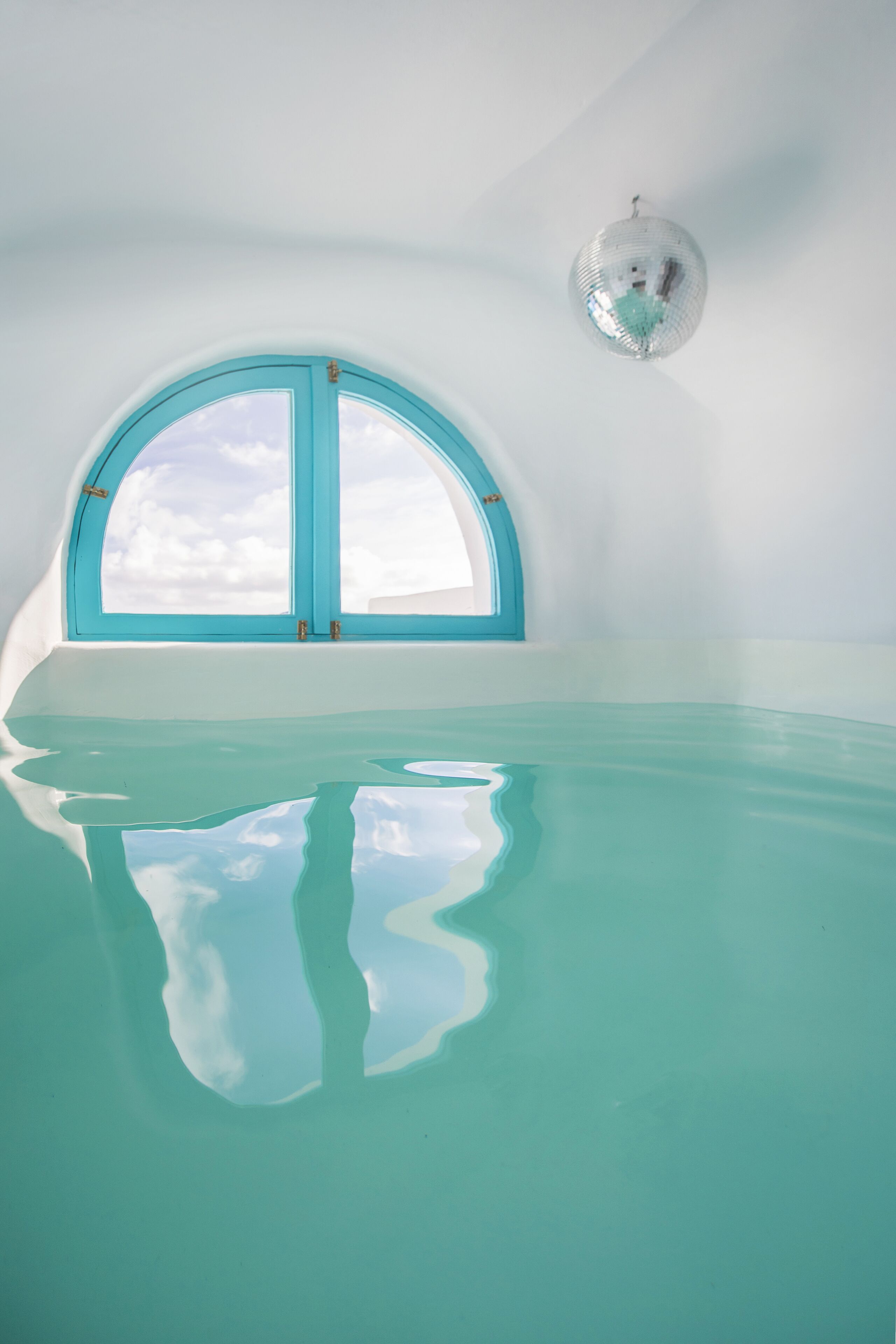 A large arched window with a teal frame, a clear view of the sky, and a disco ball hanging from the ceiling.