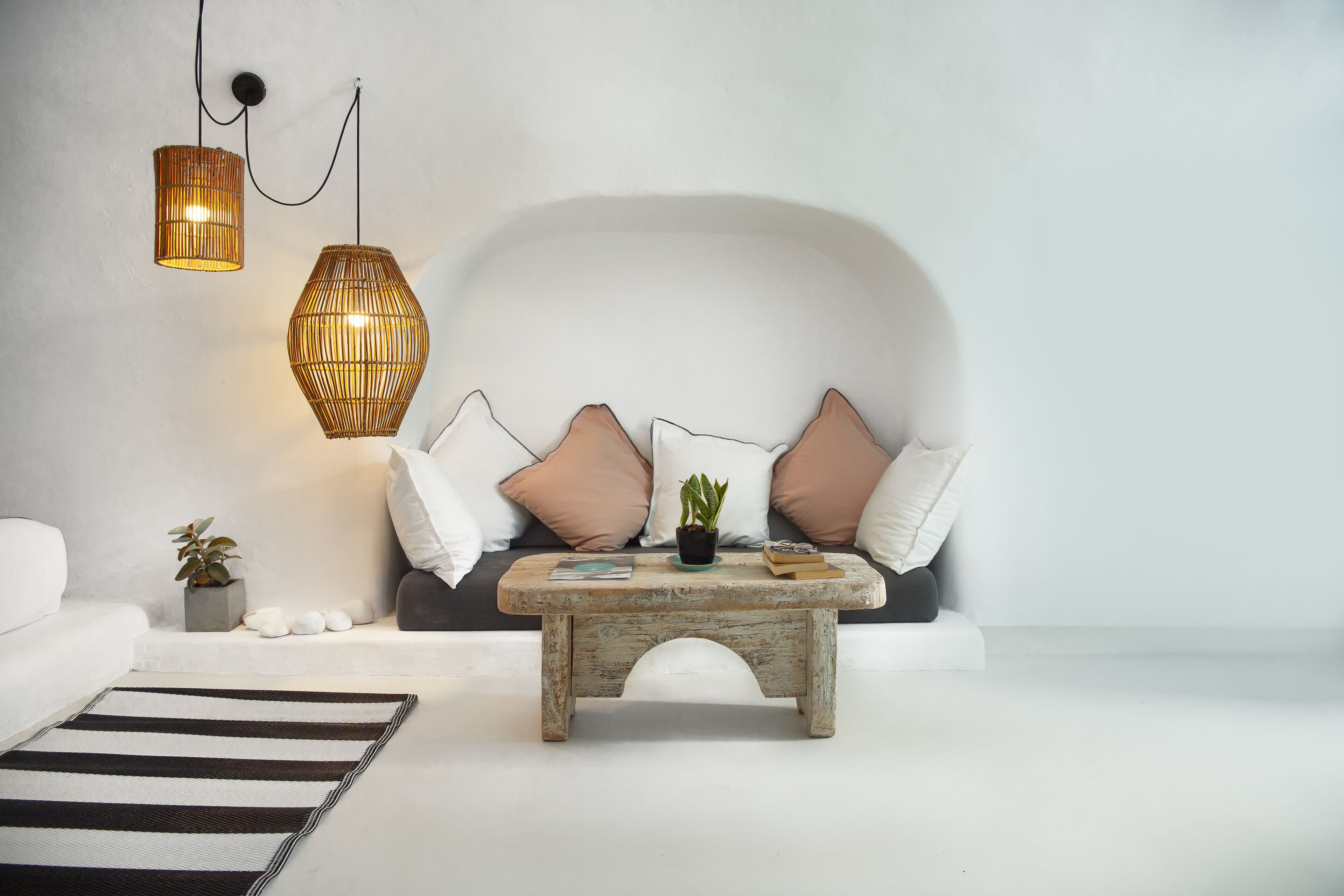 Una sala de estar moderna con un sofá blanco, una mesa de centro de madera y dos lámparas colgantes de mimbre.