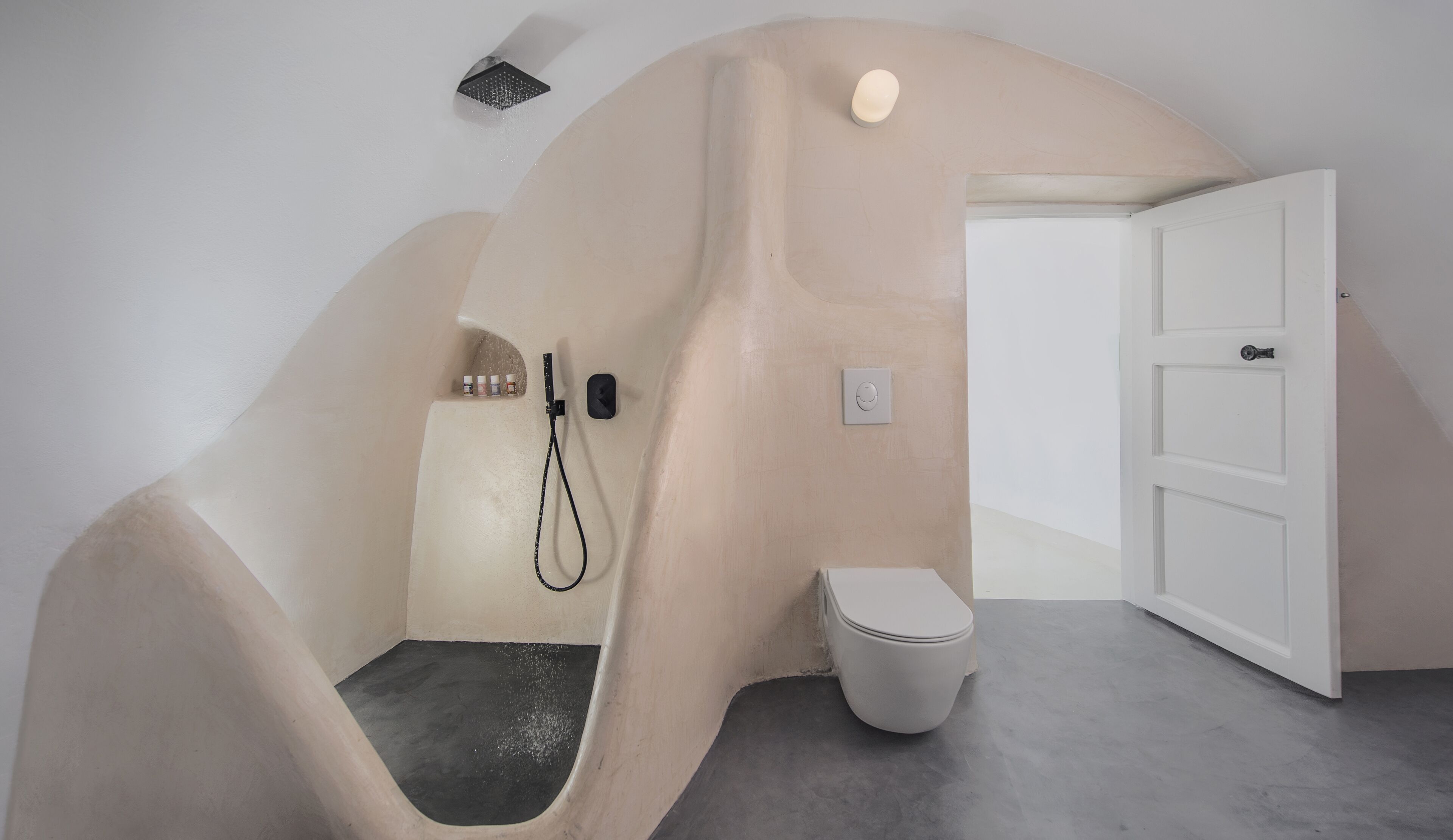 A bathroom with a unique curved design, a toilet, a shower, and a door.