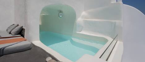 Une piscine à débordement blanche, à l’eau d’un bleu cristallin, entourée de murs blancs et d’une bordure en pierre agrémentée de sièges.